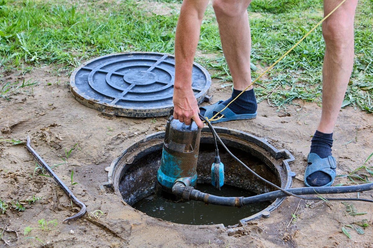 Septic tank maintenance, worker uses submersible waste water pump to pumping sewage out of tank.