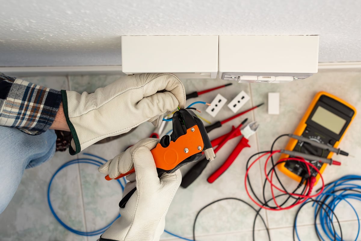 Electrician worker at work with wire stripper pliers prepares the electrical cables of an electrical system. Working safely with protective gloves. Construction industry.